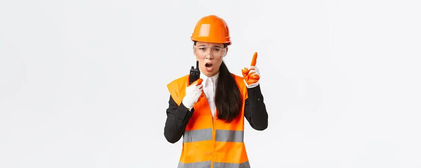 Ernst wirkende asiatische Industrieingenieurin/Technikerin mit Sicherheitshelm und Uniform an den Bedienelementen.