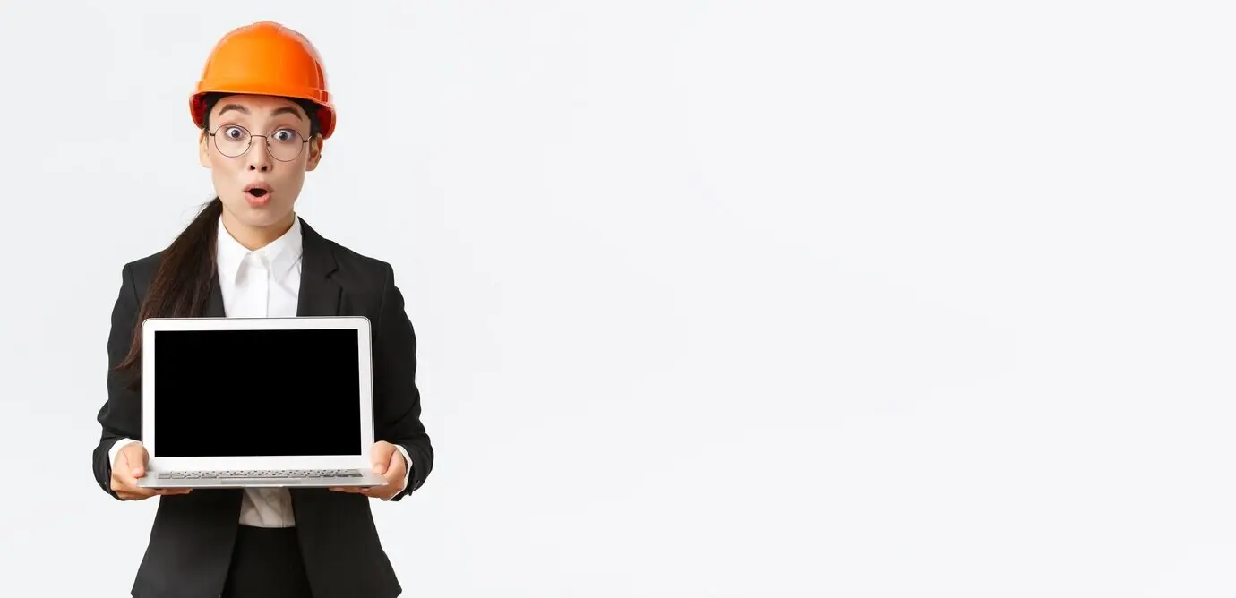 Beeindruckte und begeisterte asiatische Ingenieurin, als Industrietechnikerin mit Sicherheitshelm und Anzug, zeigt auf einem Diagramm erstaunliche Ergebnisse und präsentiert den Laptop-Bildschirm mit erstaunter Miene vor weißem Hintergrund.